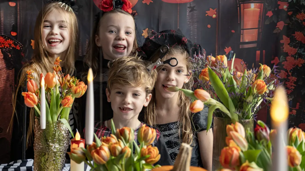 Śmiech, kostiumy i bukiety tulipanów – nawet Halloween może być kwiatowe! Dzieci przy stole pokazują, że połączenie grozy i uroku naprawdę działa.