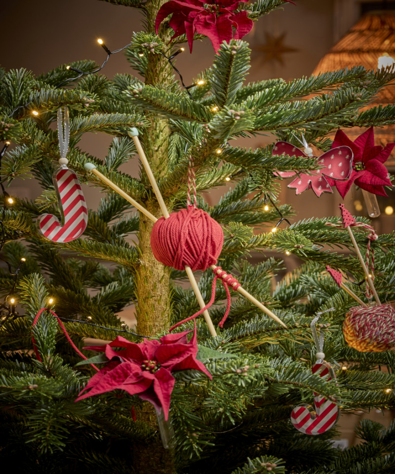 Choinka ozdobiona czerwonymi poinsecjami, włóczką z drutami i zawieszkami w stylu rękodzieła