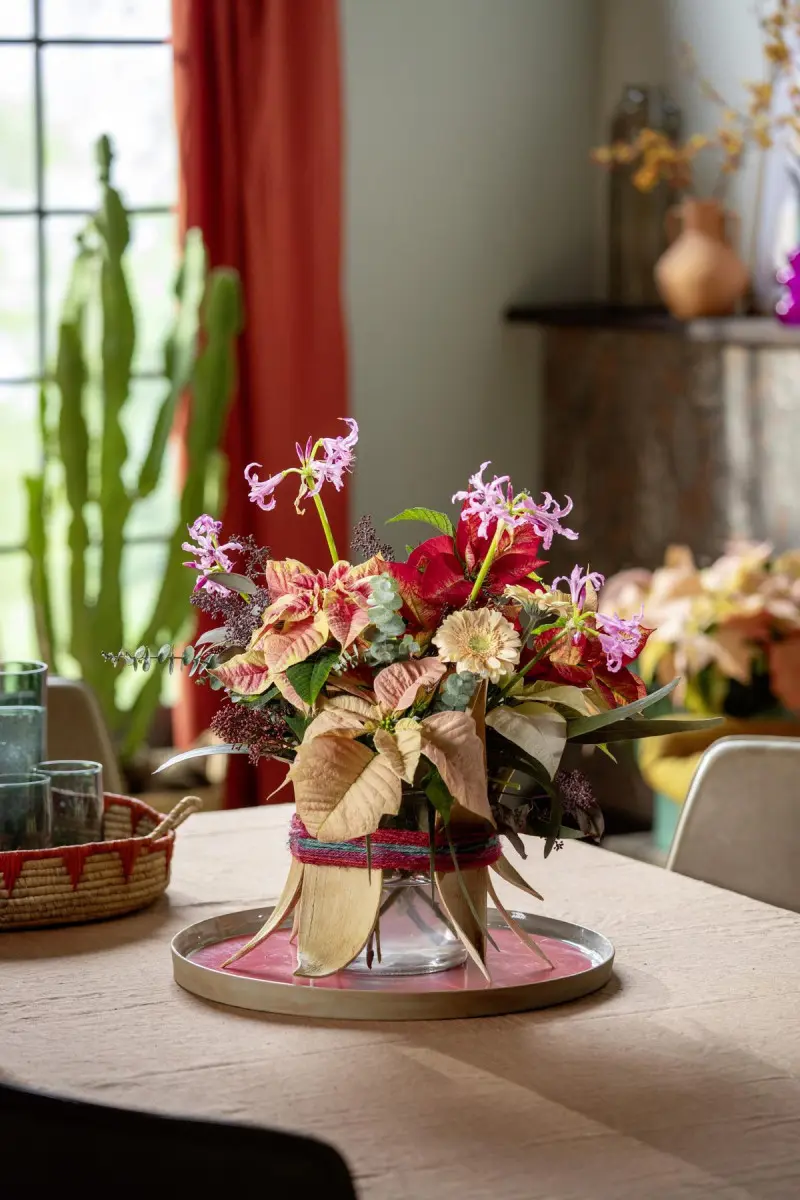 Bukiet z poinsecji i sezonowych kwiatów w szklanym wazonie, ustawiony na stole w salonie