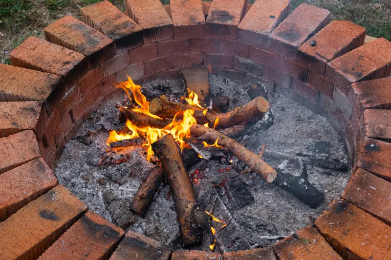 Ognisko zbudowane z klasycznych czerwonych cegieł – prosty i efektowny sposób na wieczory w ogrodzie przy płomieniach.