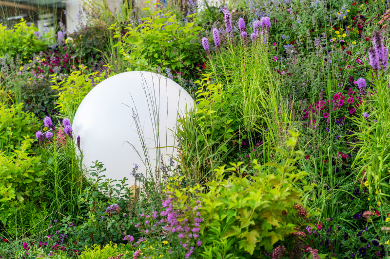 Lampa ogrodowa w kształcie kuli na rabacie z trawami i bylinami – dekoracyjne oświetlenie ogrodu w ciągu dnia