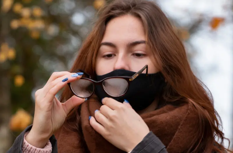 Okulary zaparowane podczas noszenia maseczki – kobieta sprawdza zamglone szkła na zewnątrz.