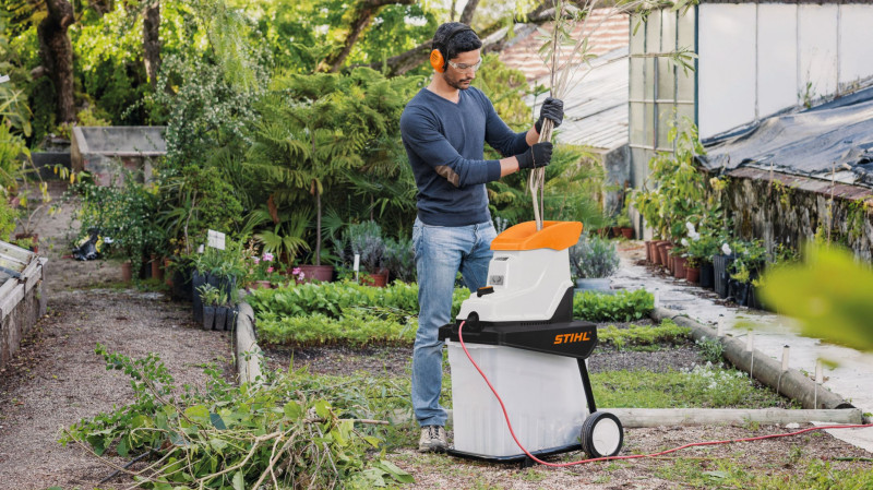Mężczyzna rozdrabnia gałęzie w ogrodzie za pomocą rozdrabniacza STIHL, przygotowując odpady do kompostowania.