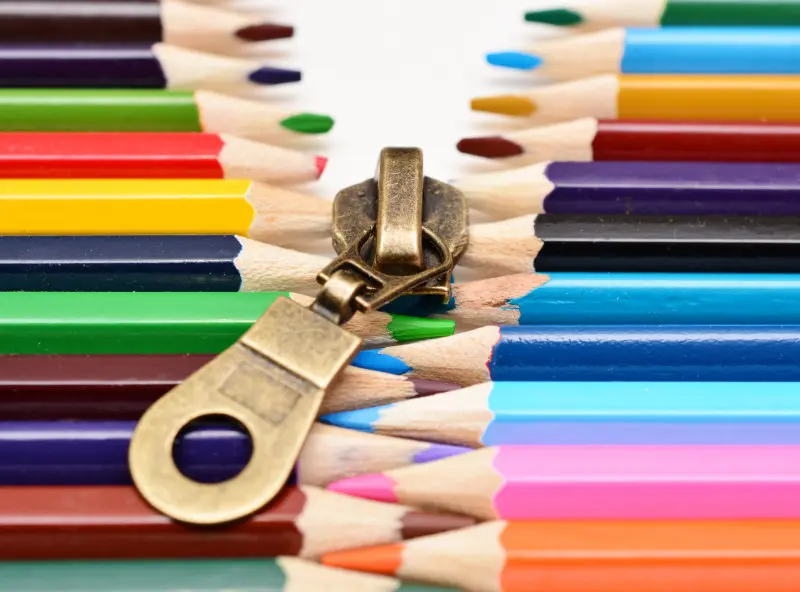 Metalowy suwak zamka wśród kolorowych kredek – przykład, dlaczego kredki nie zastąpią grafitu z ołówka.