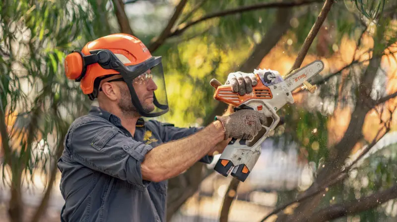 Mężczyzna w kasku i ochronie oczu przycina gałęzie piłą akumulatorową STIHL GTA 40.