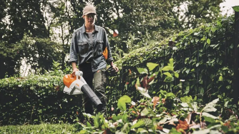 Kobieta sprząta liście w ogrodzie za pomocą akumulatorowej dmuchawy STIHL.
