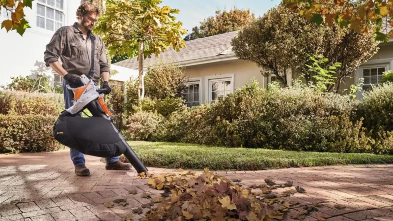 Mężczyzna sprząta liście z podjazdu za pomocą odkurzacza ogrodowego STIHL z workiem na odpady.