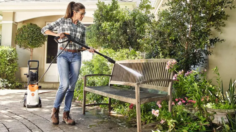 Kobieta czyści ławkę ogrodową za pomocą myjki ciśnieniowej STIHL RE 100 PLUS Control.