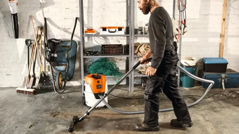 Mężczyzna sprząta podłogę w garażu za pomocą odkurzacza na mokro i sucho STIHL SE 62E.