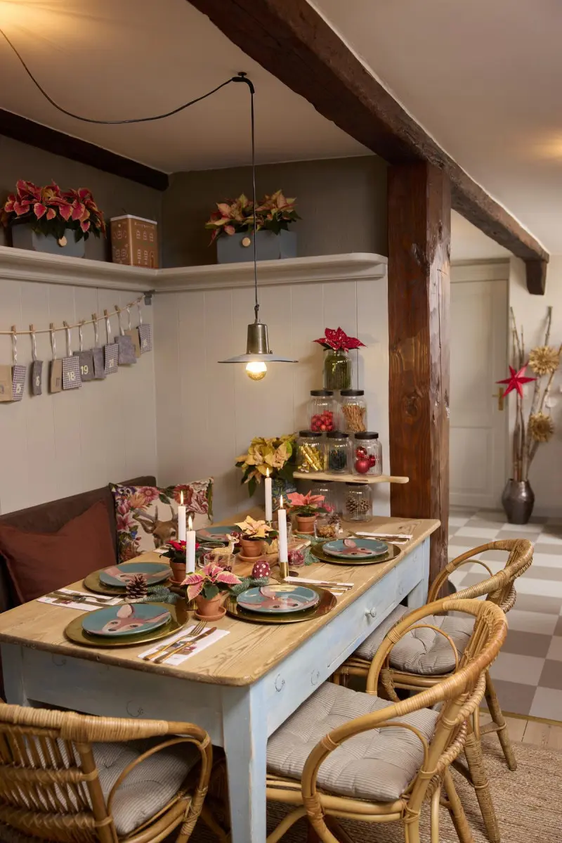 Przytulna jadalnia w stylu rustykalnym z bożonarodzeniowym stołem udekorowanym poinsecjami, świecami i talerzami z motywem jelonka.