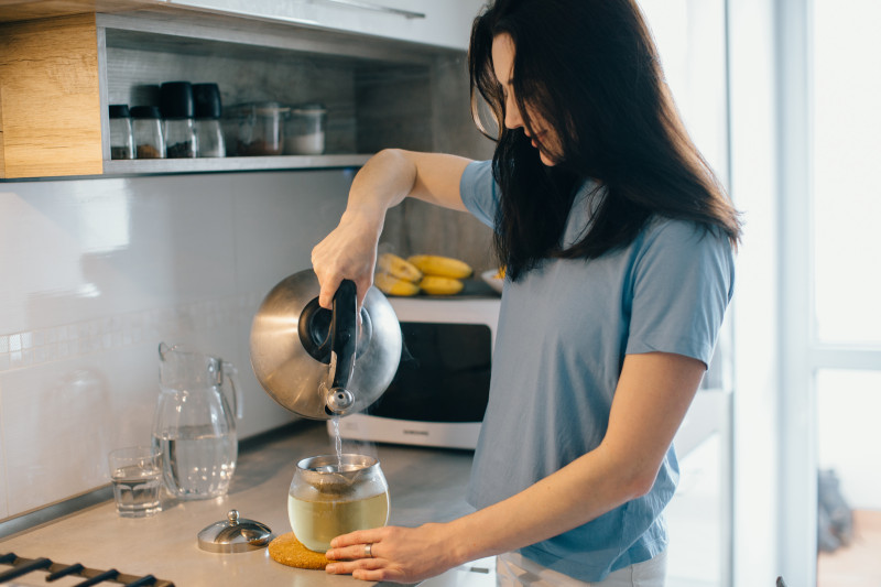 Kobieta zalewa ziołową herbatę wrzątkiem – zaparzanie jesiennej herbaty z ogrodu.