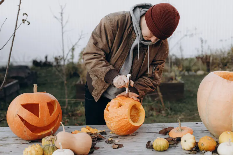 Mężczyzna wycina wzory w dyni na Halloween – klasyczny lampion z dyni jako tradycyjna dekoracja jesienna