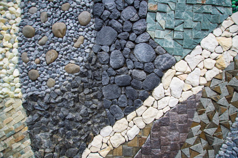 Dekoracyjna mozaika z kamieni w ogrodzie – otoczaki, grys i łupki ułożone w kontrastowe pasy jako ozdobna nawierzchnia