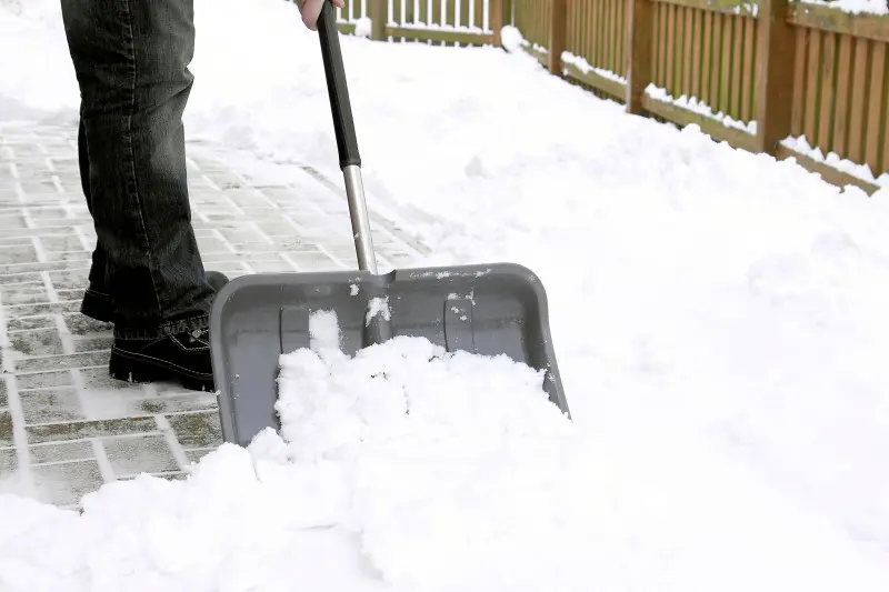 Osoba odśnieżająca chodnik plastikową łopatą w zimowy dzień